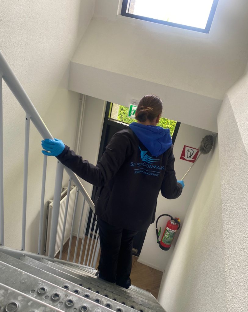 Medewerker van SD Schoonmaakdienst in bedrijfskleding stoft een trappenhuis af