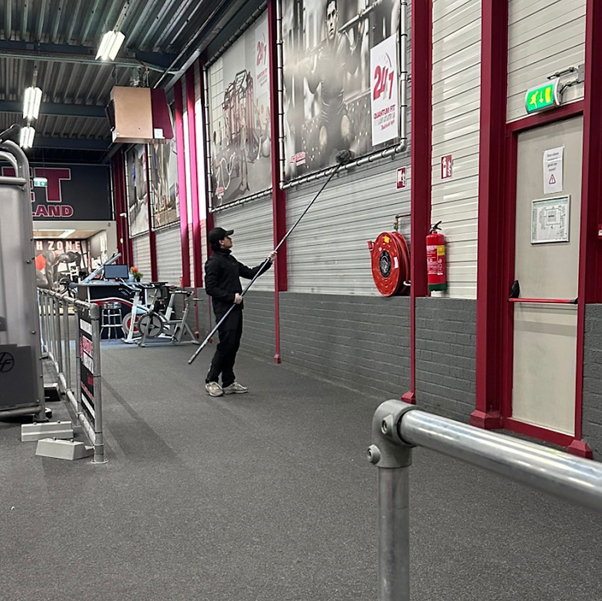 Medewerker van SD Schoonmaakdienst maakt met een telescoopsteel hoog werk schoon in een sportschool