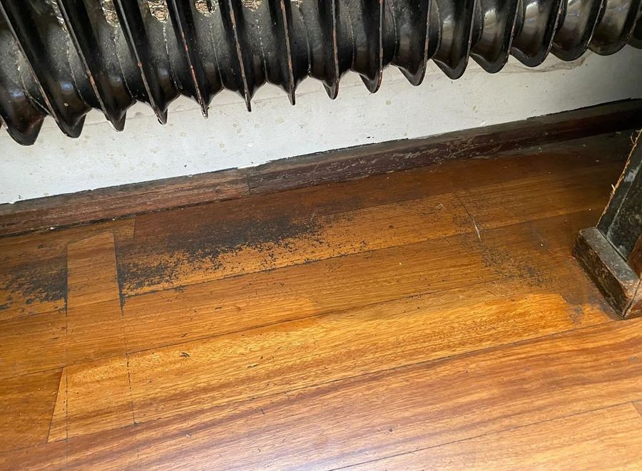 Houten vloer langs de radiator, vóór de schoonmaak: vuil en dof