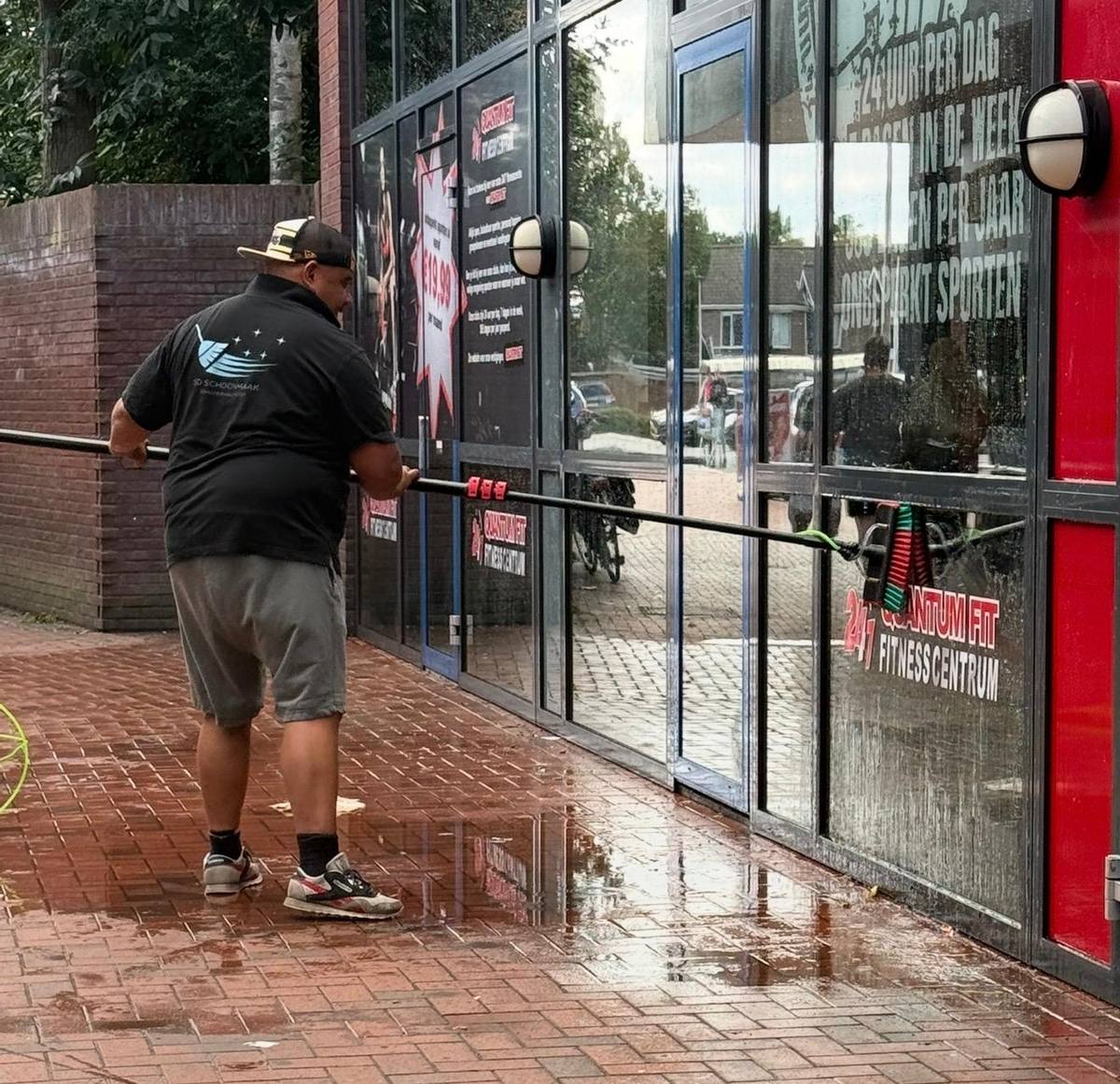 Glazenwasser van SD Schoonmaakdienst wast de ramen van een sportschool met een telescoopsteel